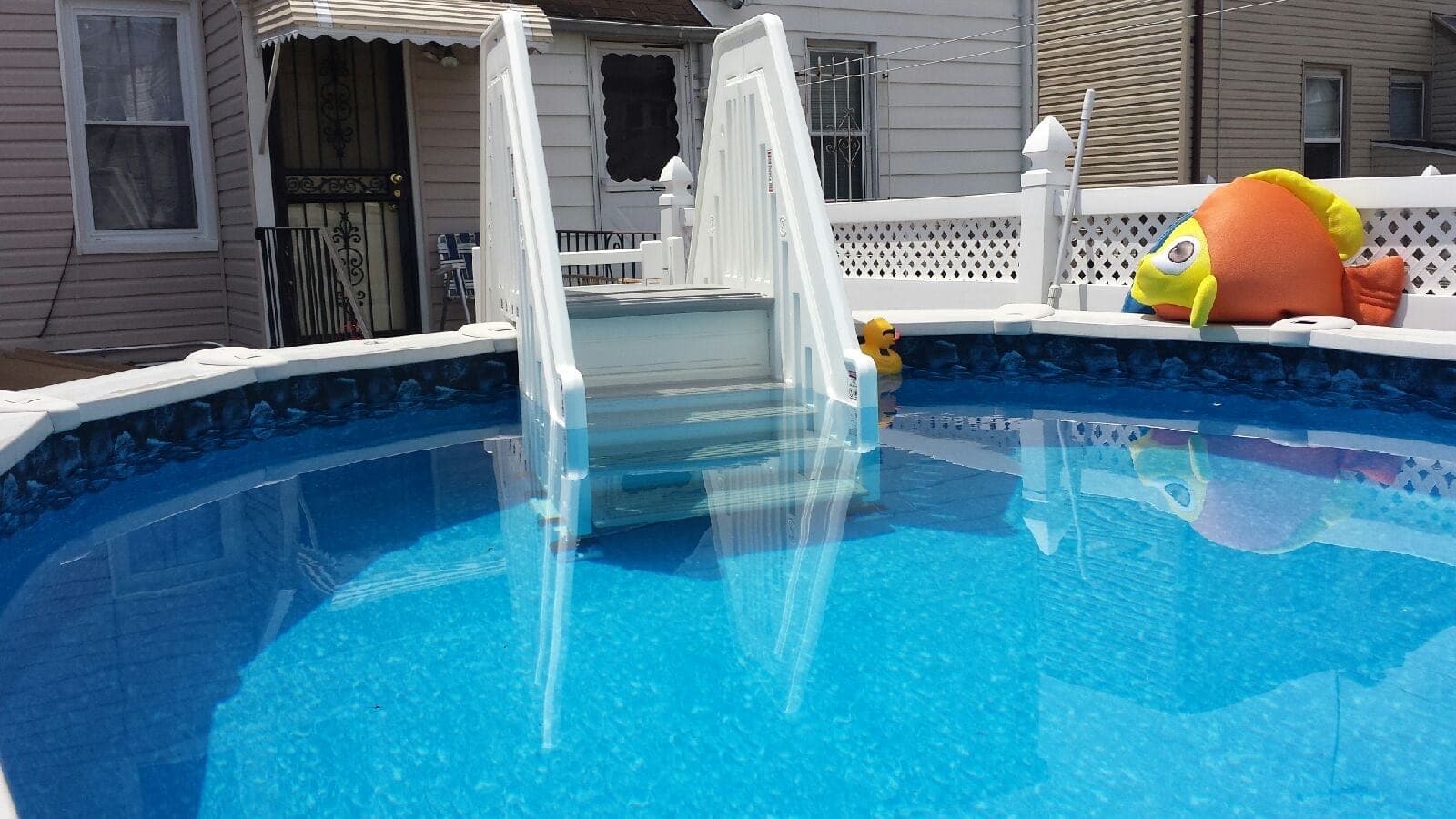 Entry steps with white handrails set into a pool wall, seen across the water, a rock-pattern liner border and a lattice fence behind.