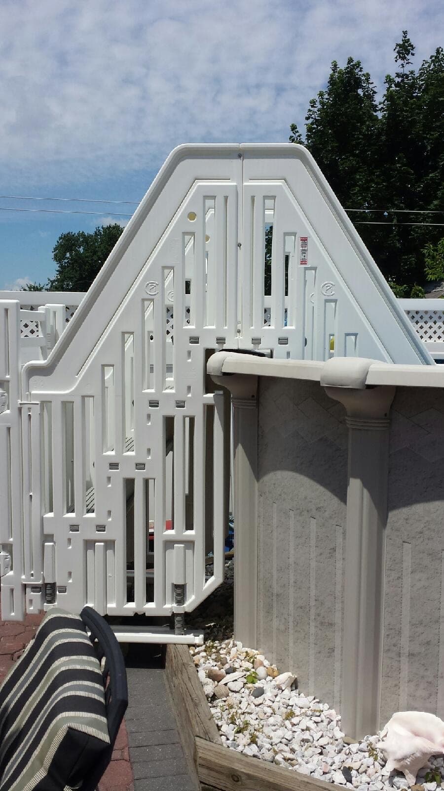 Close view of an entry system's outer gate and A-frame rail, fixed against a grey pool wall above a gravel bed.