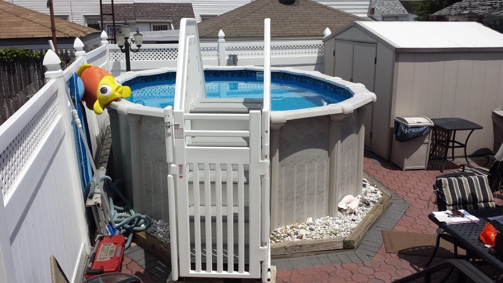 Round pool from above, the gated entry system standing at the near wall with the vacuum hose and pole alongside.
