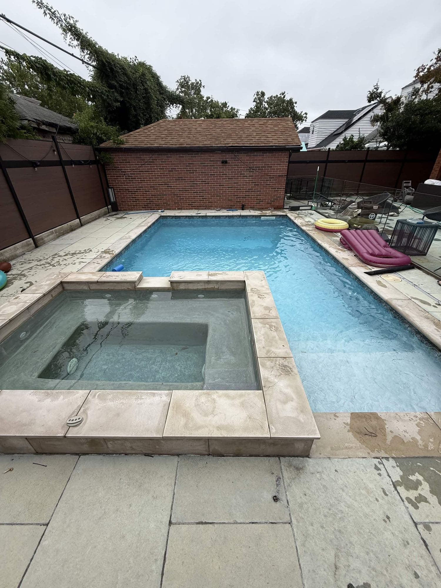 In-ground pool with attached raised spa and stone coping, backing a brick pool house.