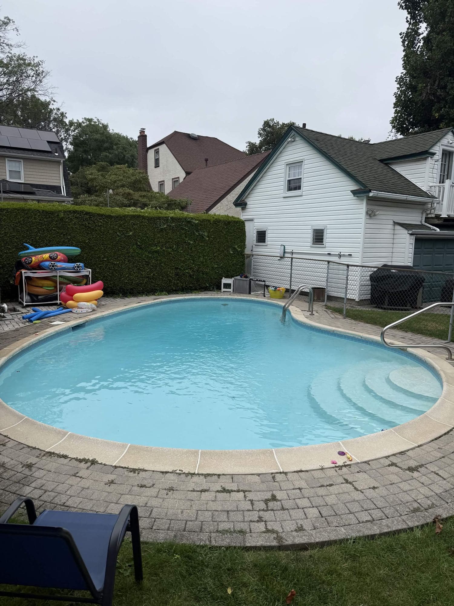 Kidney-shaped in-ground pool with tan interior finish, set into a paved backyard.