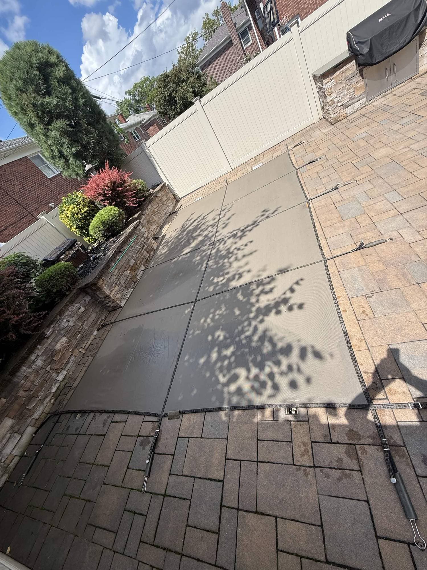 Overhead view of a paved pool patio with a taut mesh safety cover in place over the water.