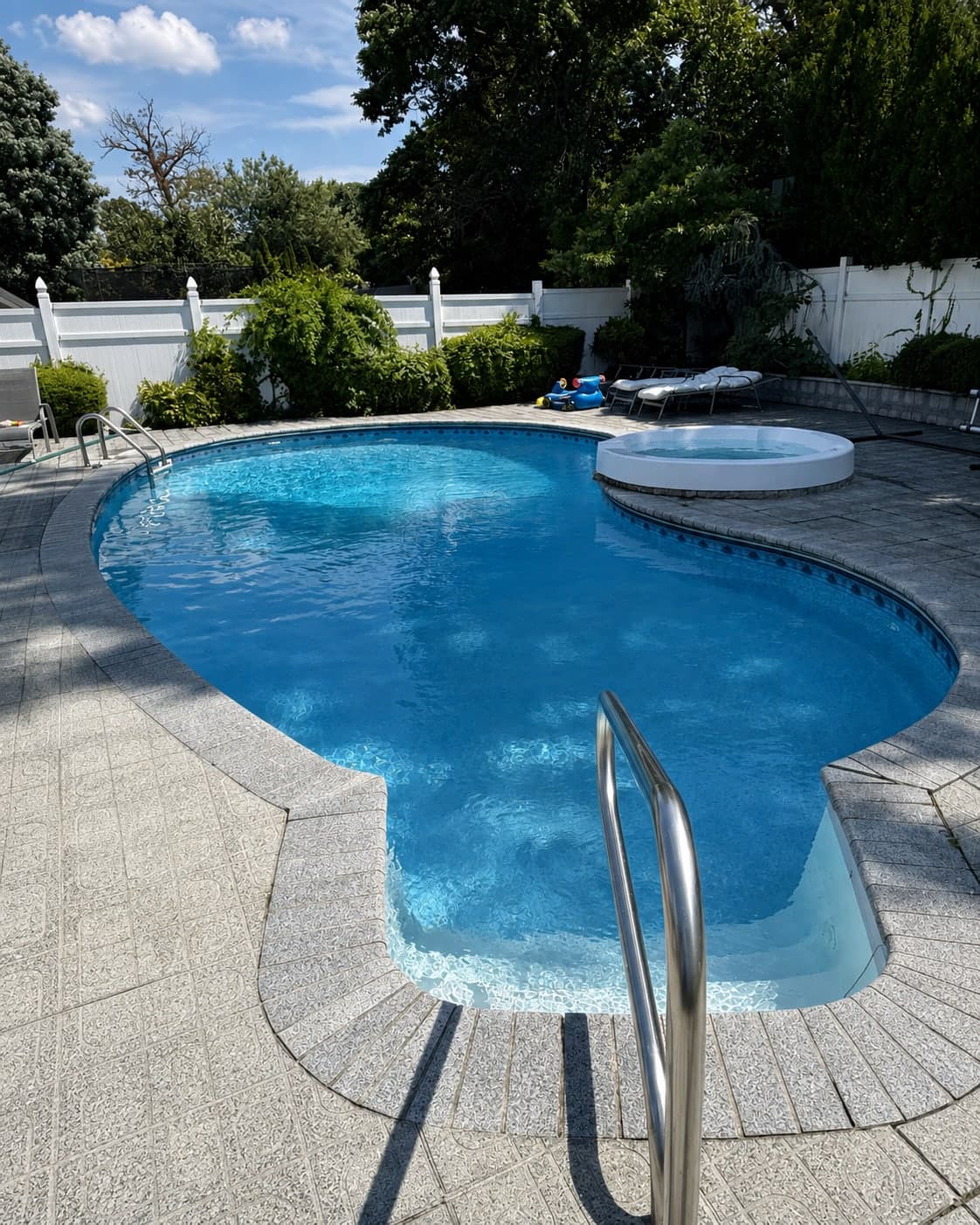Freeform inground pool with an attached round spa, set in a light aggregate patio